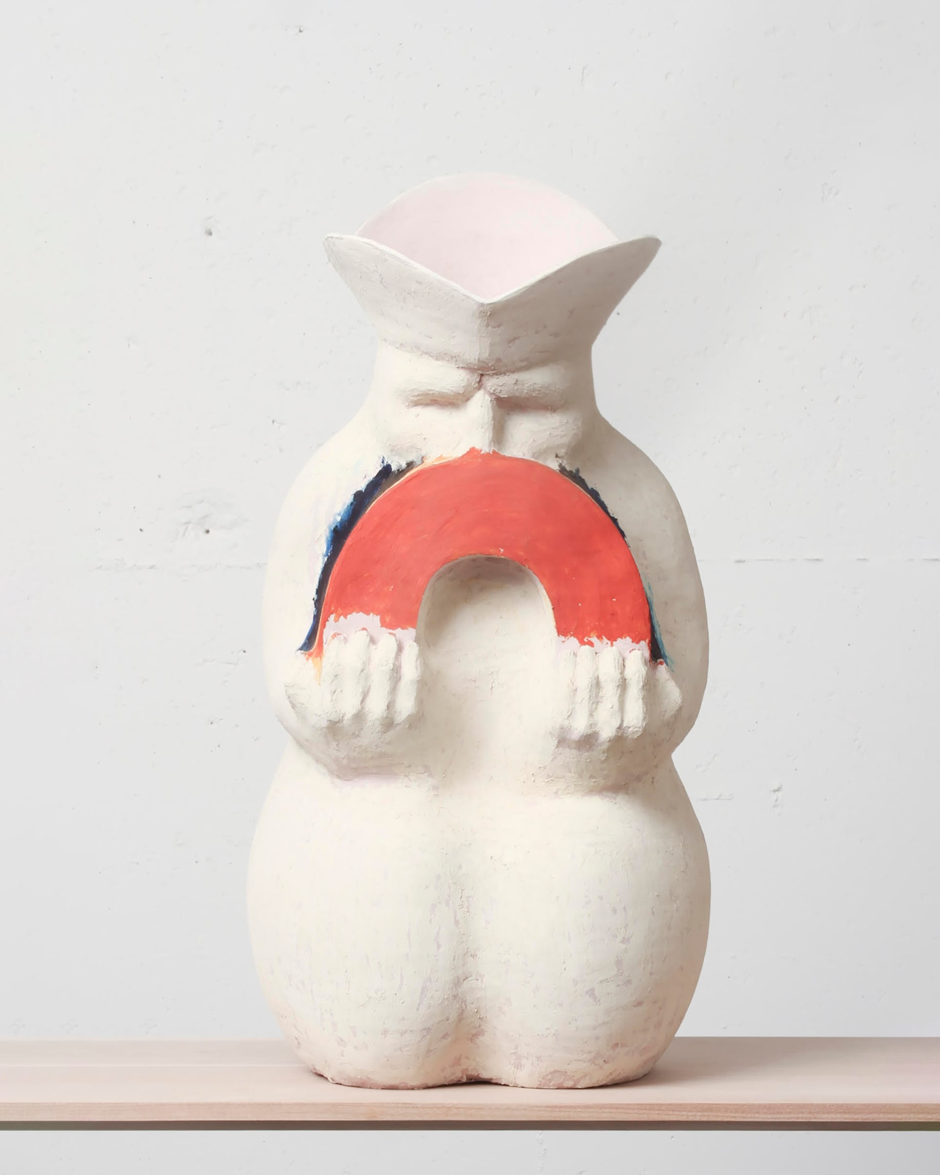 A hollow white ceramic sculpture of a man holding a rainbow. 