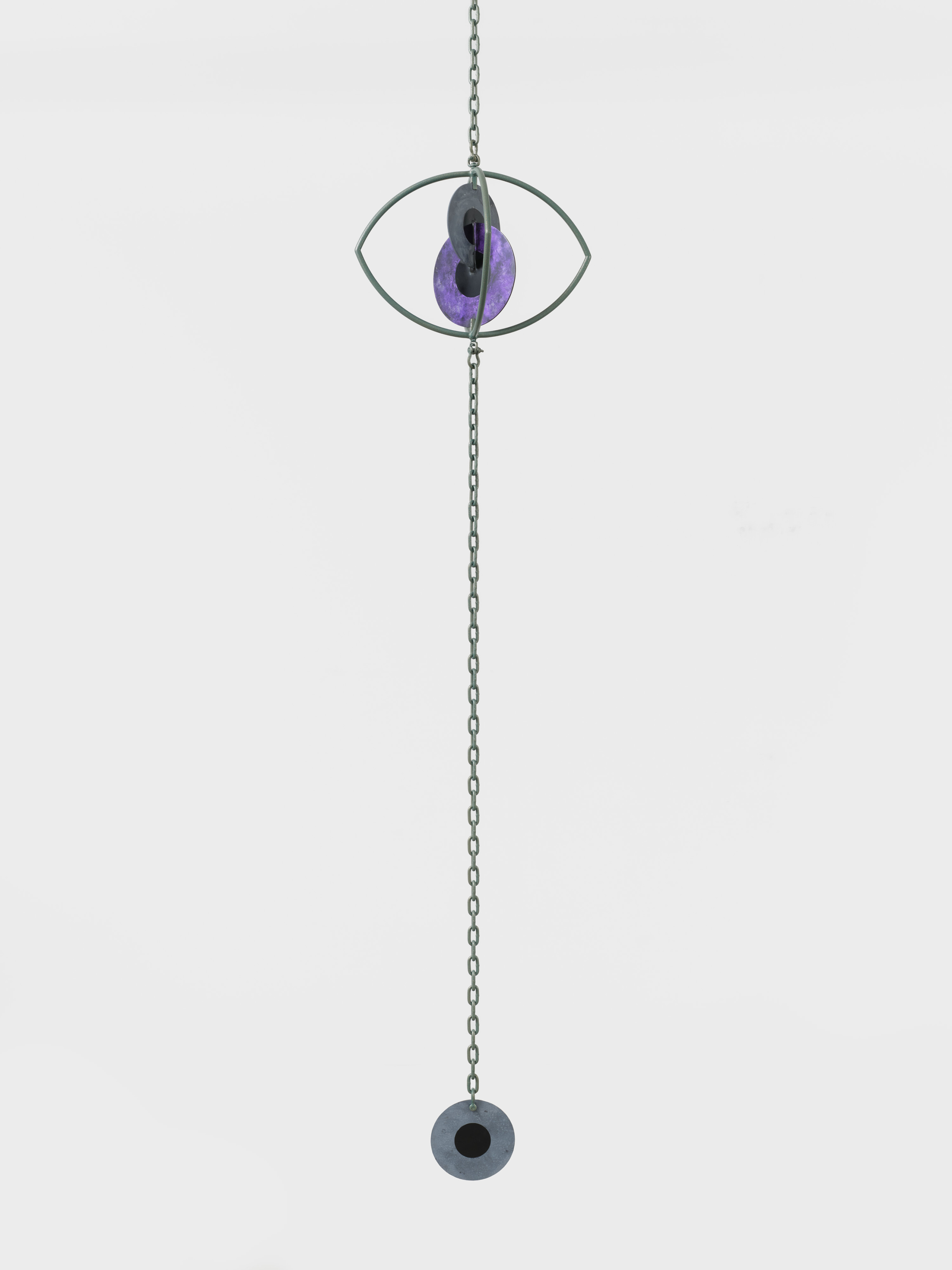 A hanging sculpture with two interlocking metal iris' inside a metal eye with a third iris hanging from a chain. 