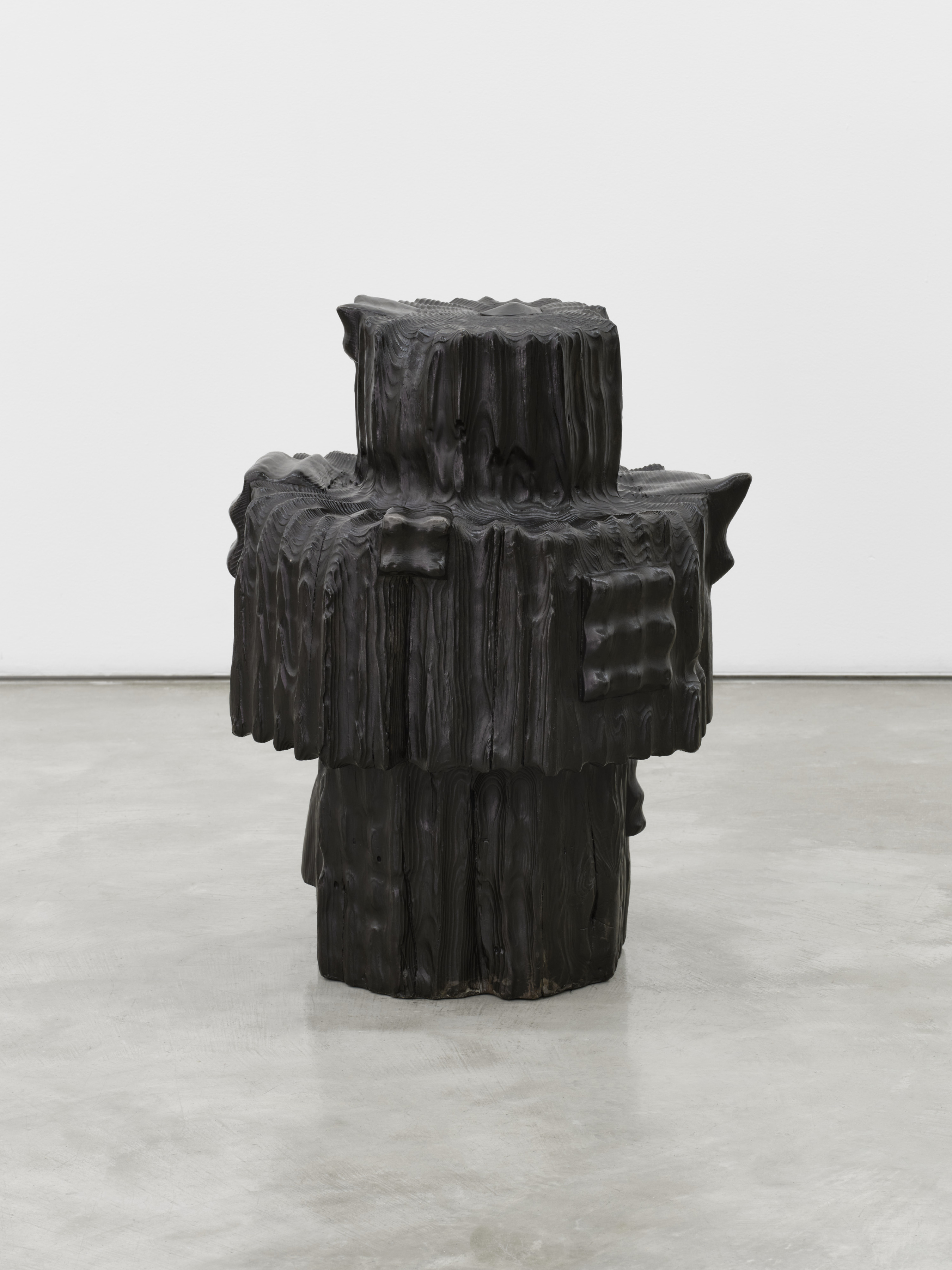 A black bronze stool-like sculpture with a protruding carving in the center.