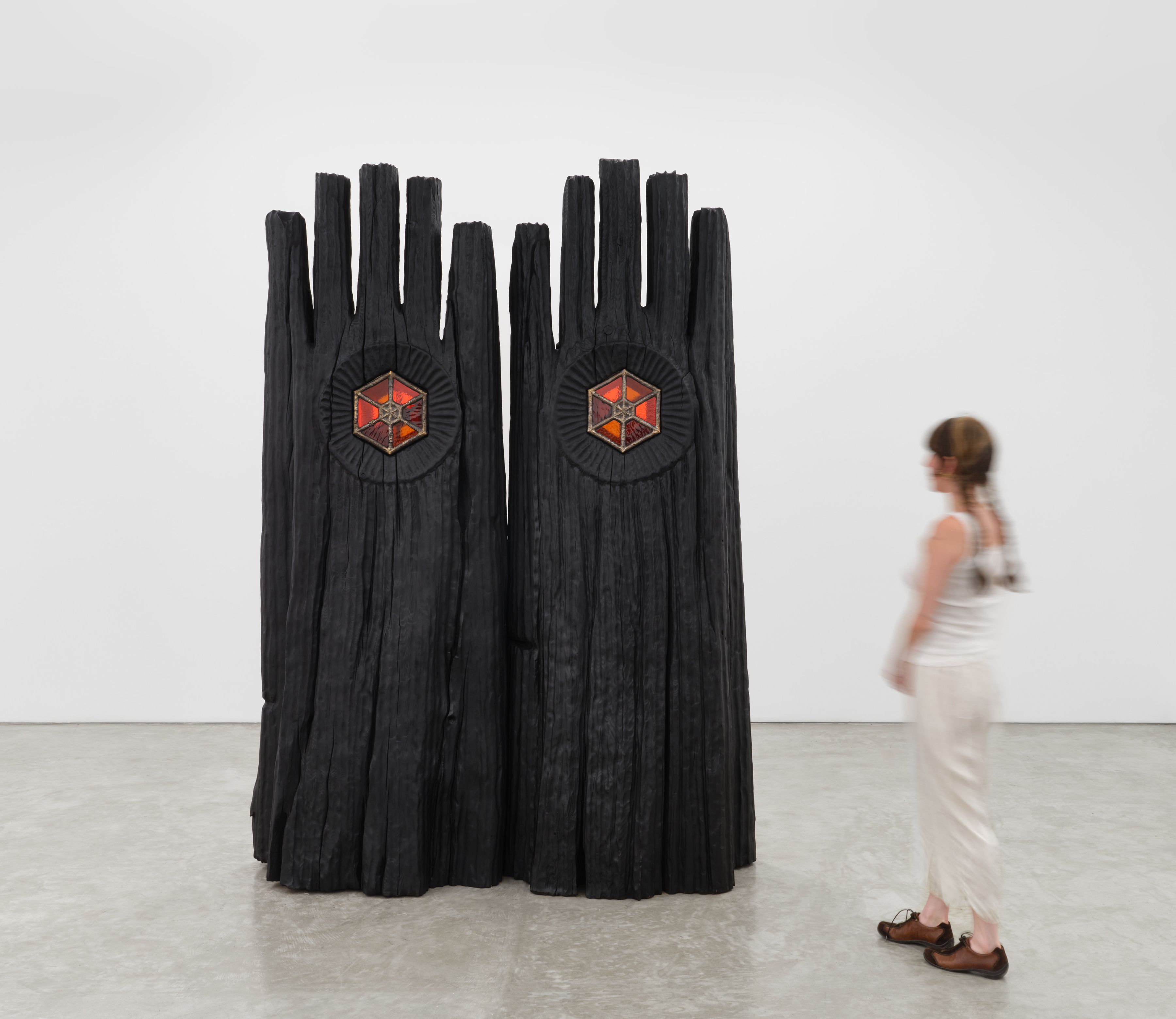 A cedar wood sculpture of two large hands painted black with red and orange stained glass windows at the center of each palm.