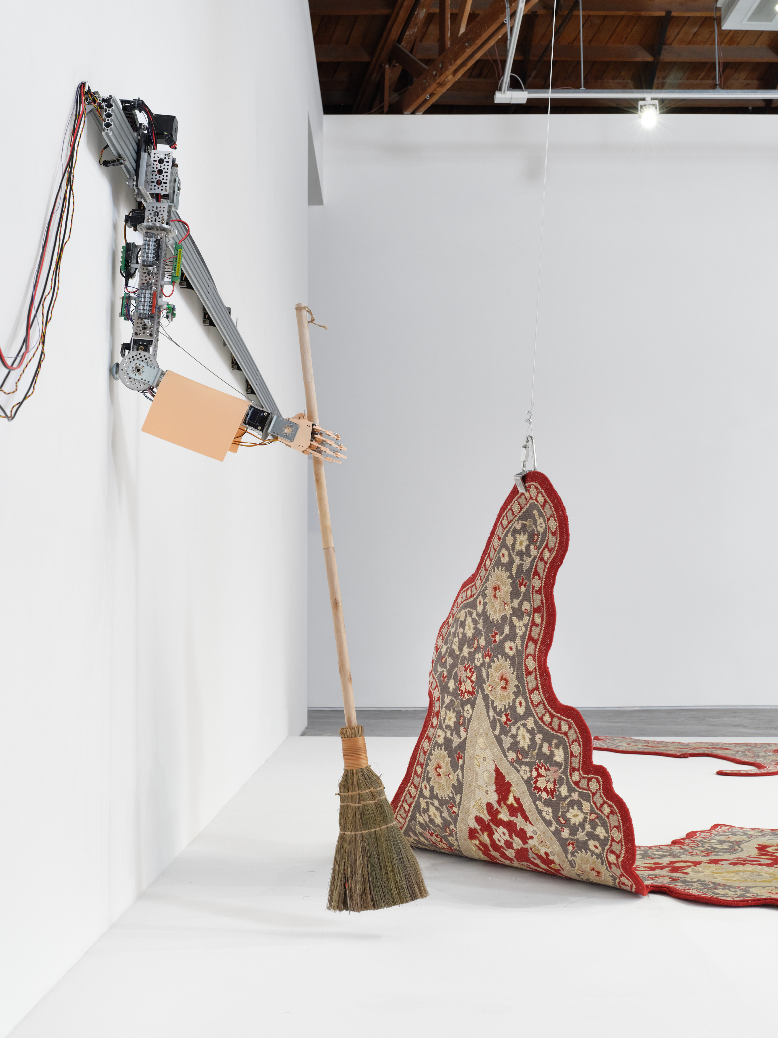 Detail of the robotic arm sweeping under the rug in Divya Mehra's "You're Doing the Work (Diamond Jubilee)", 2024