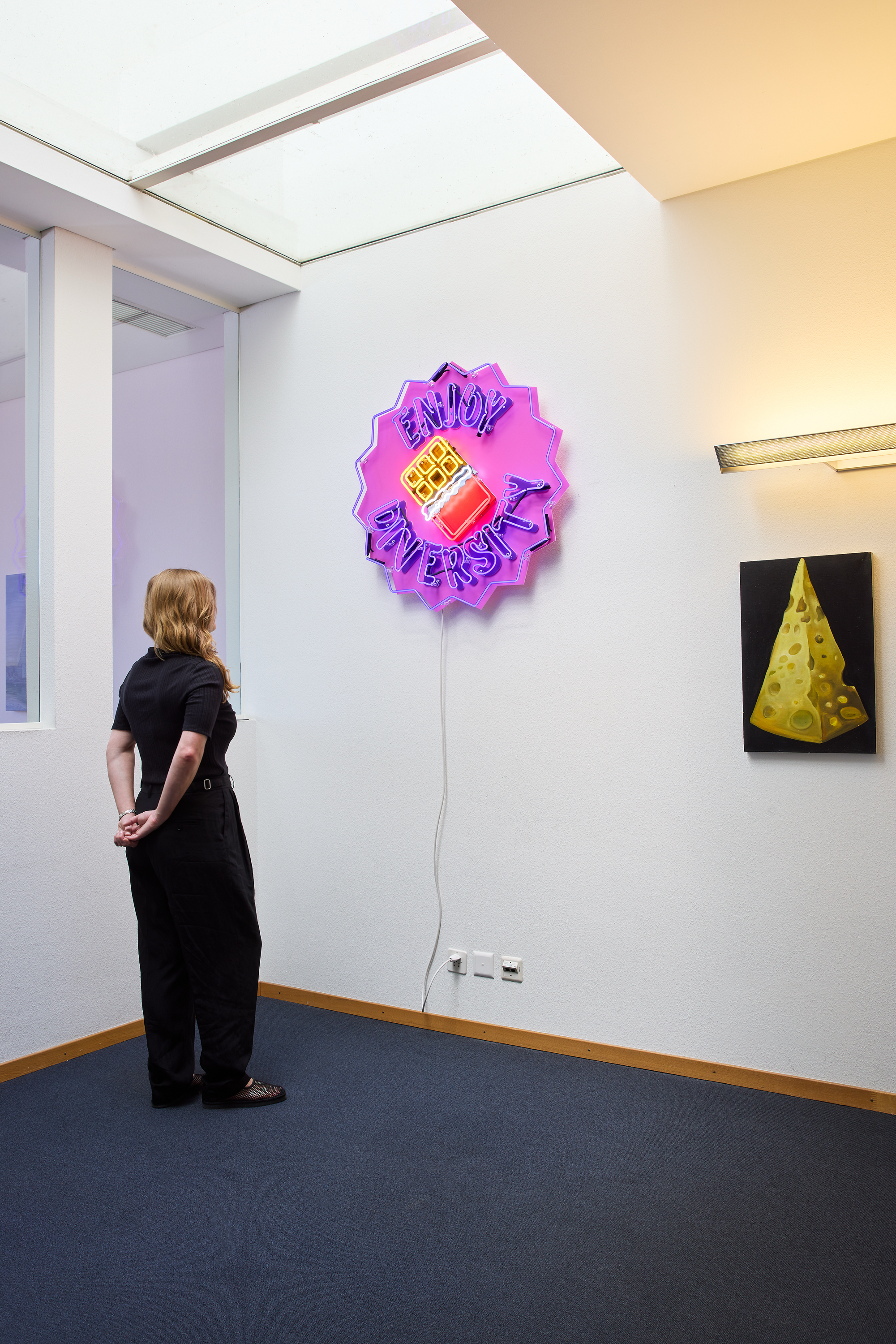 Neon work that reads "Enjoy Diversity" installed on the wall at the Basel Social Club with a person for scale. 