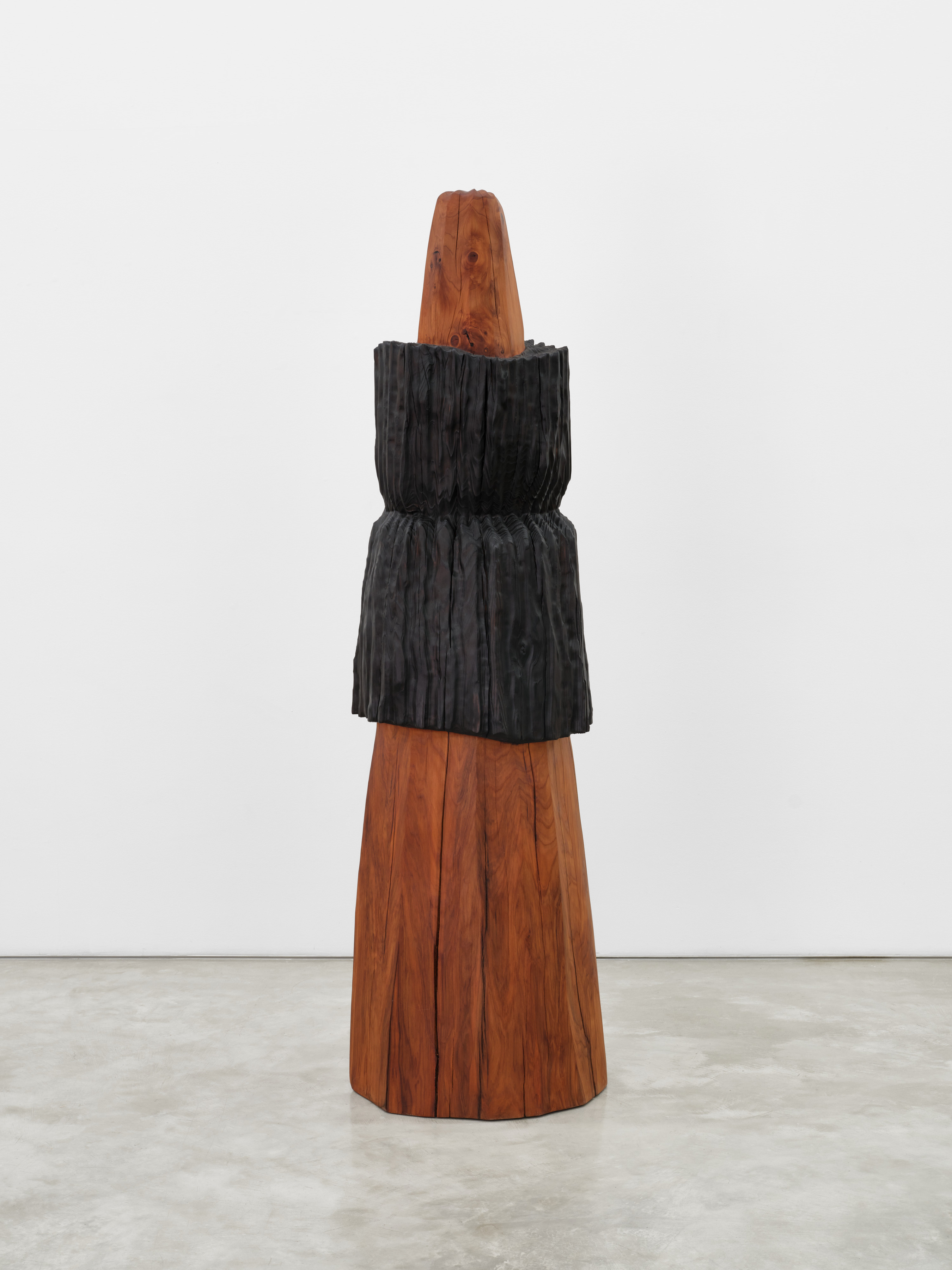 An elongated wooden cone shaped sculpture with a long black wooden carving fitted around its center.