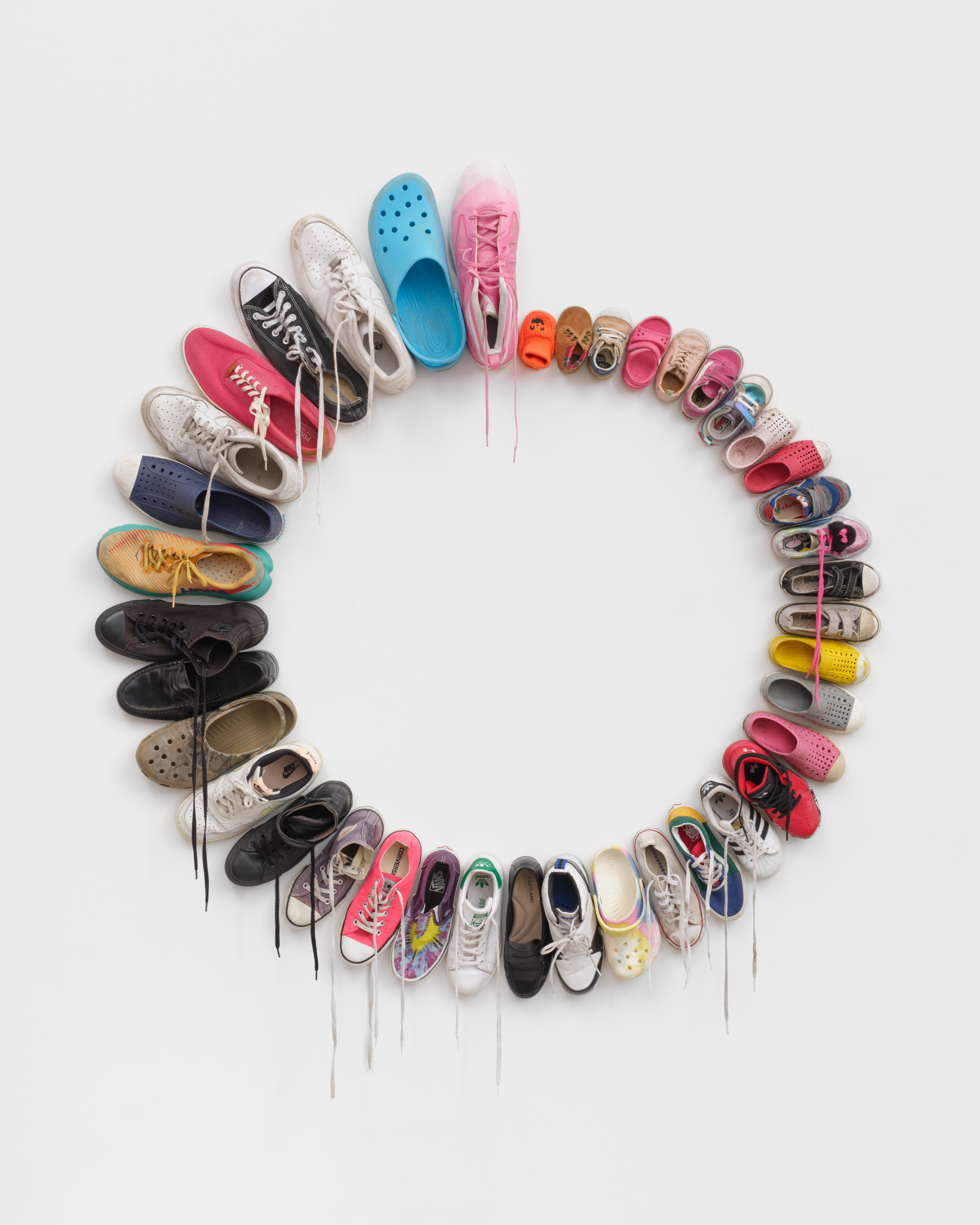 A wall mounted sculpture of shoes in a circle starting with a baby's slipper and increasing in size around the circle. 