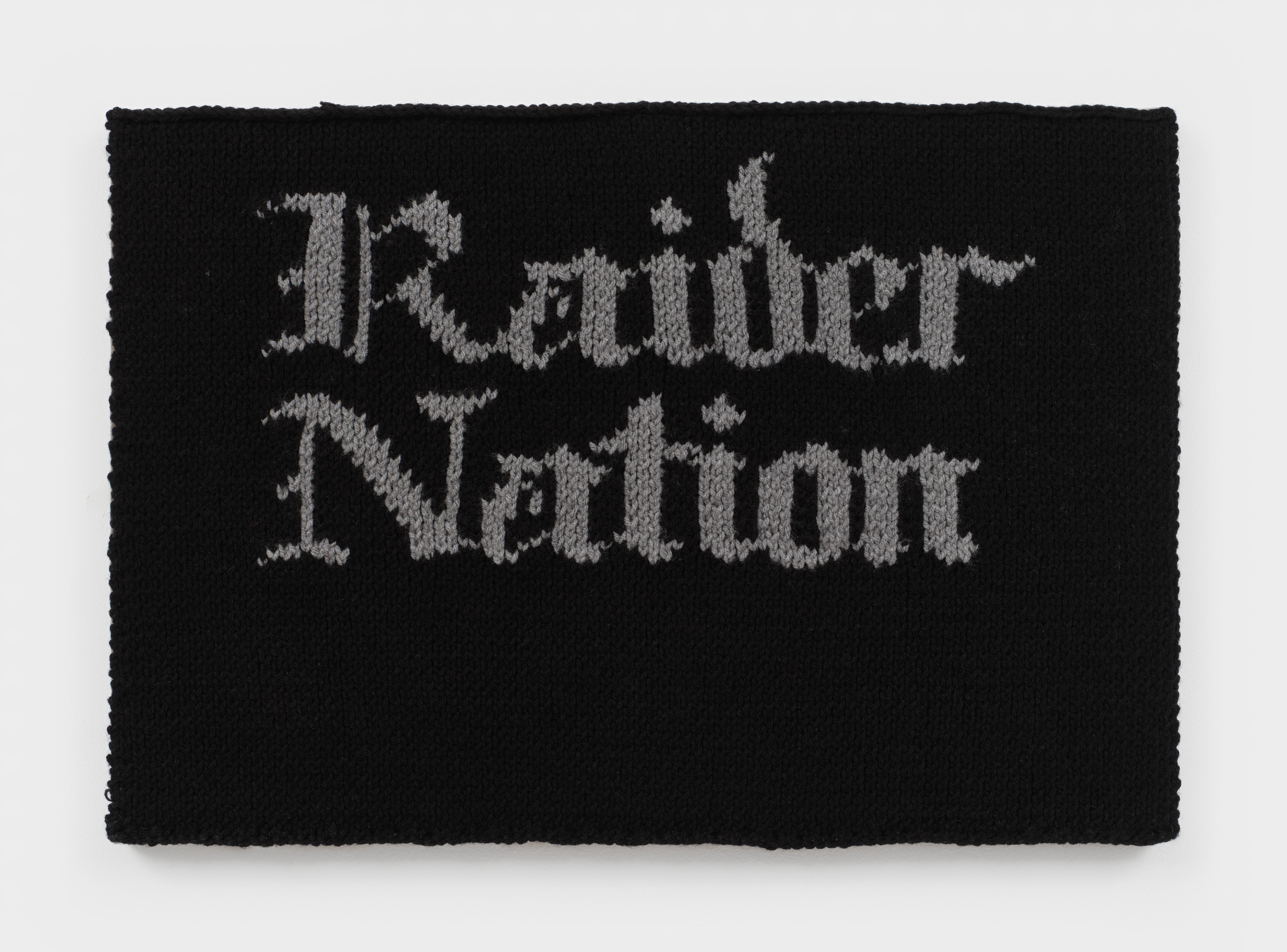 A knit artwork with the words "Raider Nation" in grey against a black background, sewn onto linen and stretched.