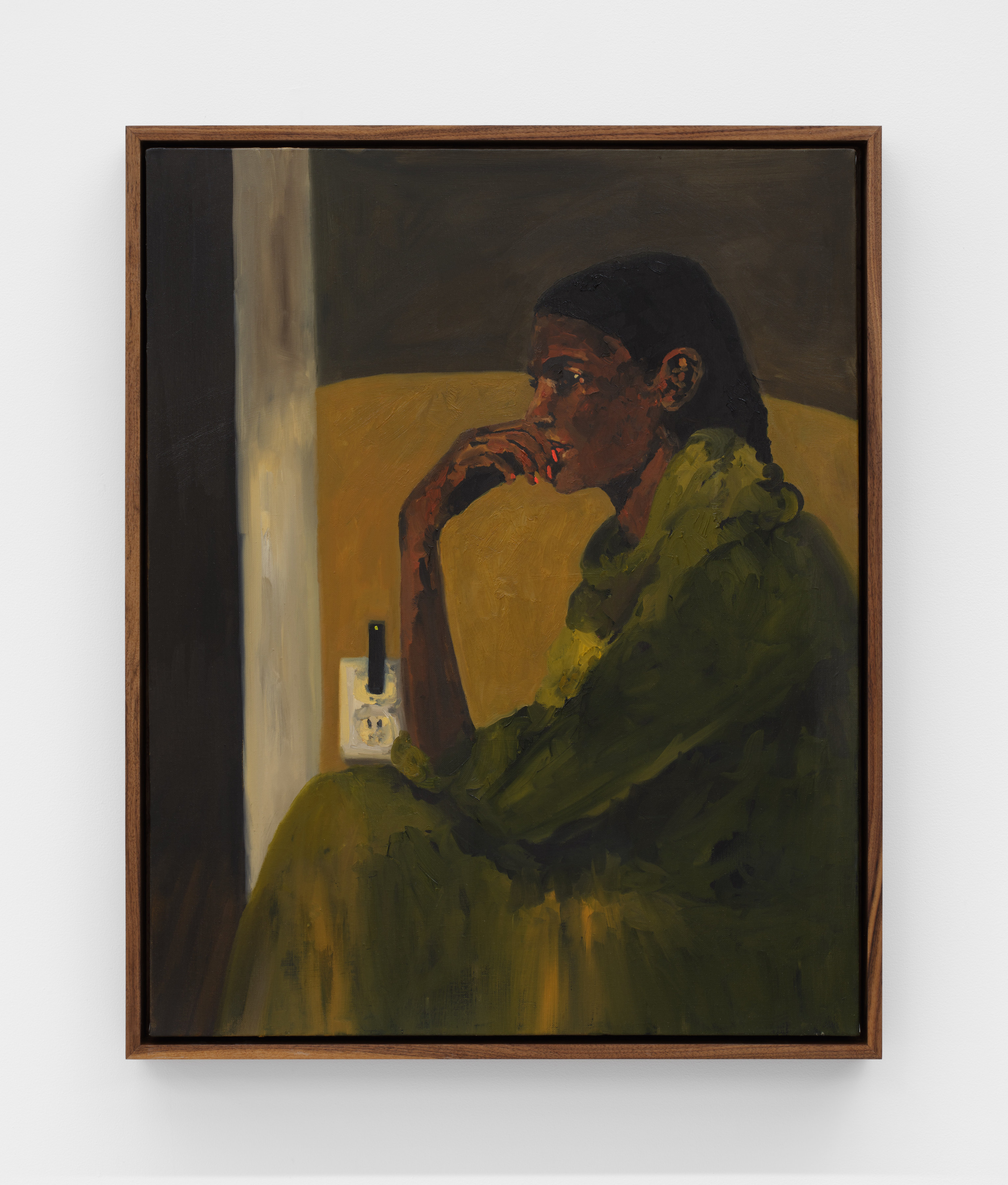 A woman wearing a forest green dress sits contemplatively with her hand to her lips while her juul charges in an outlet. 