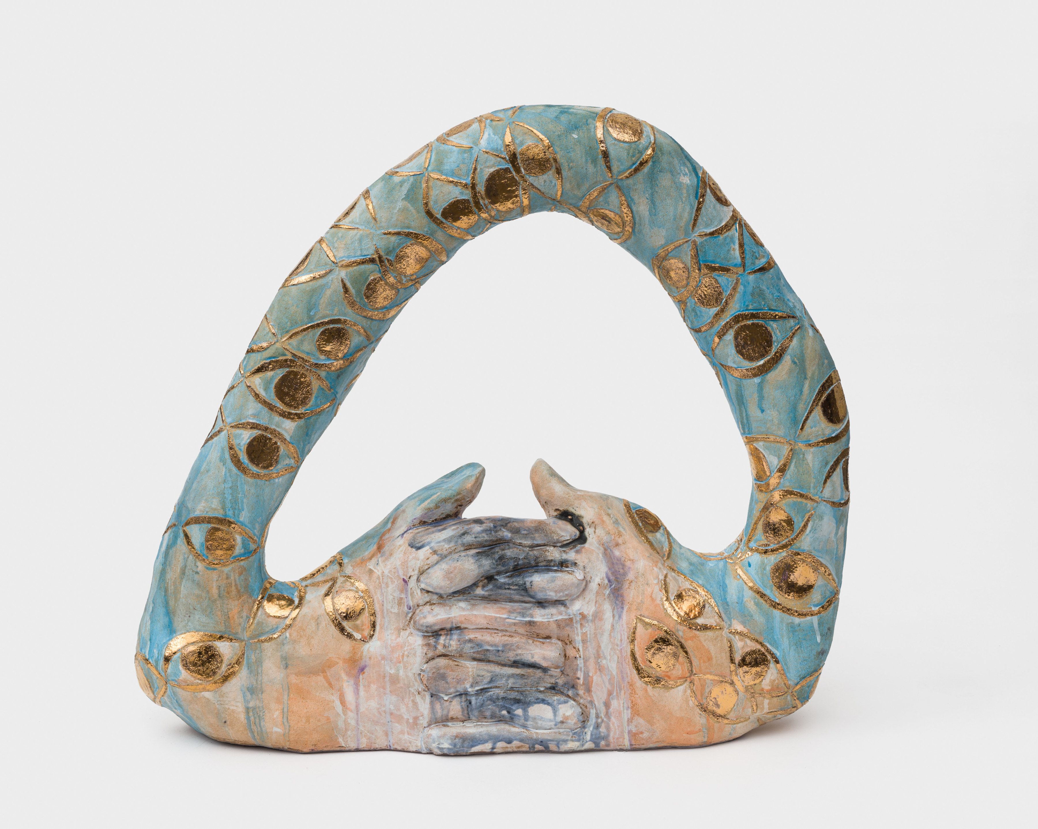 A ceramic sculpture with a base of interlocked orange glazed hands with blue glazed arms arching above with golden eyes. 