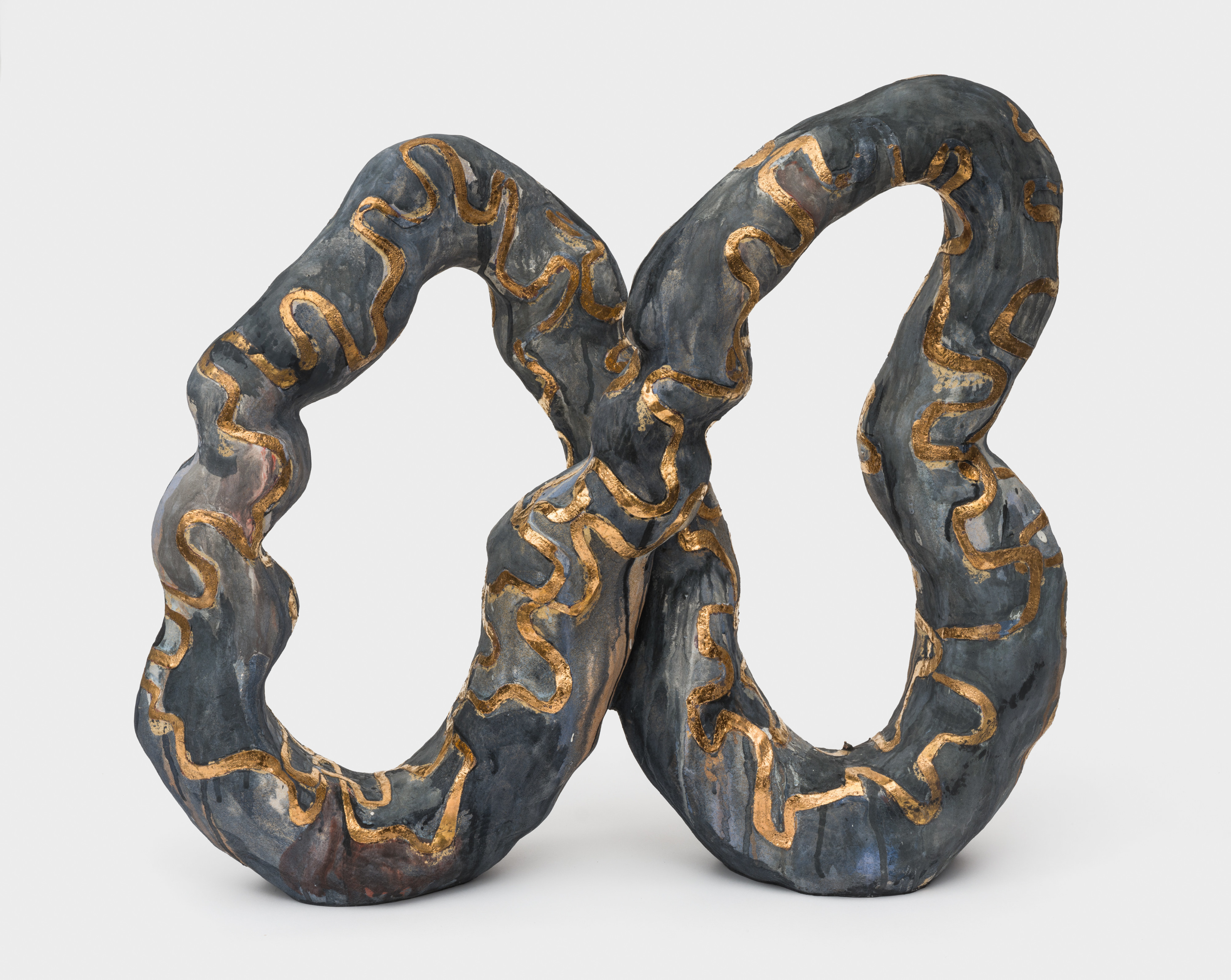 A dark grey glazed ceramic sculpture in the shape of an infinity symbol with golden details. 