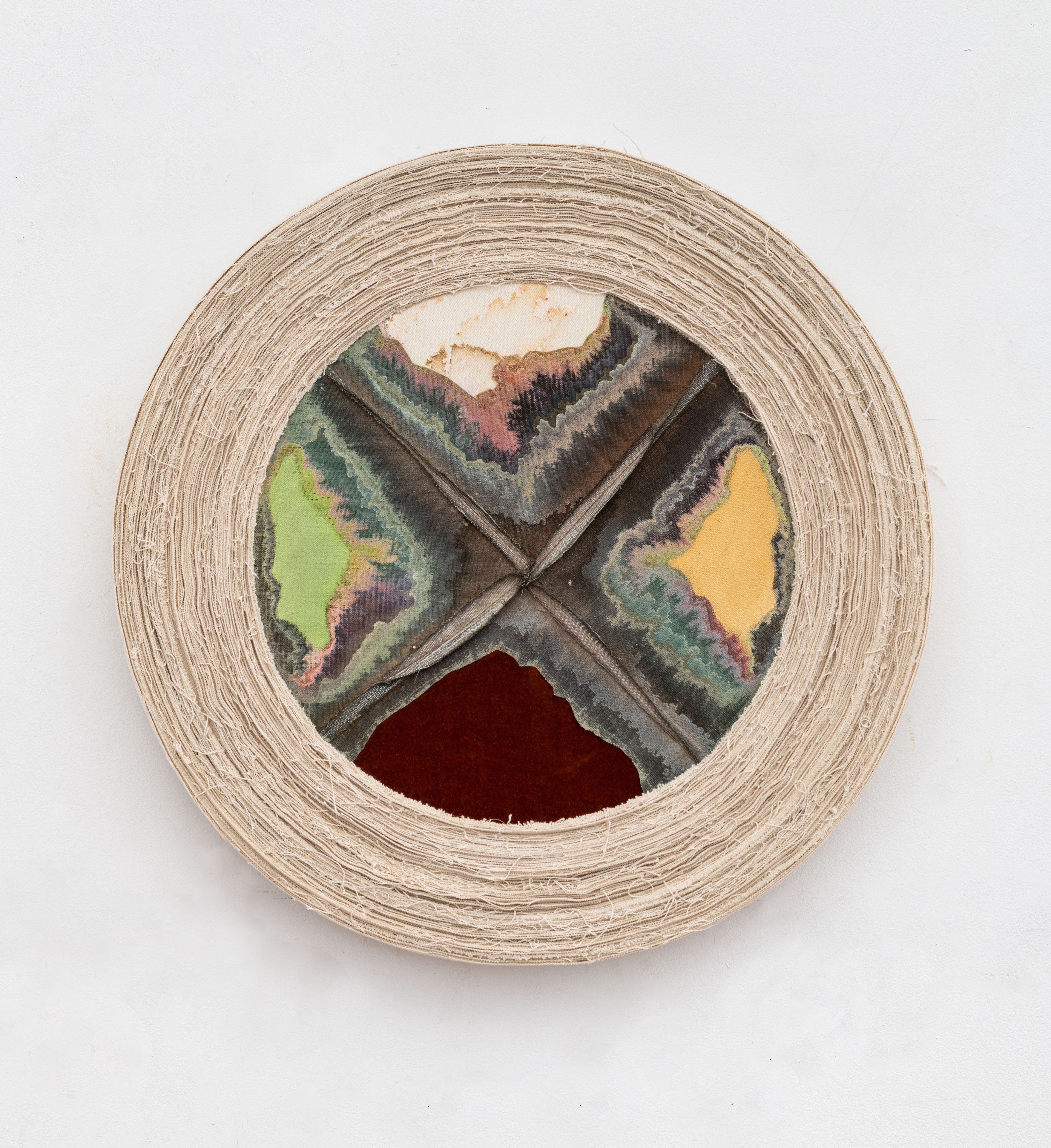A tondo painting with the canvas sewn into four segments with bleeding green, burgundy and yellow pigments wrapped in unprimed canvas on the periphery. 