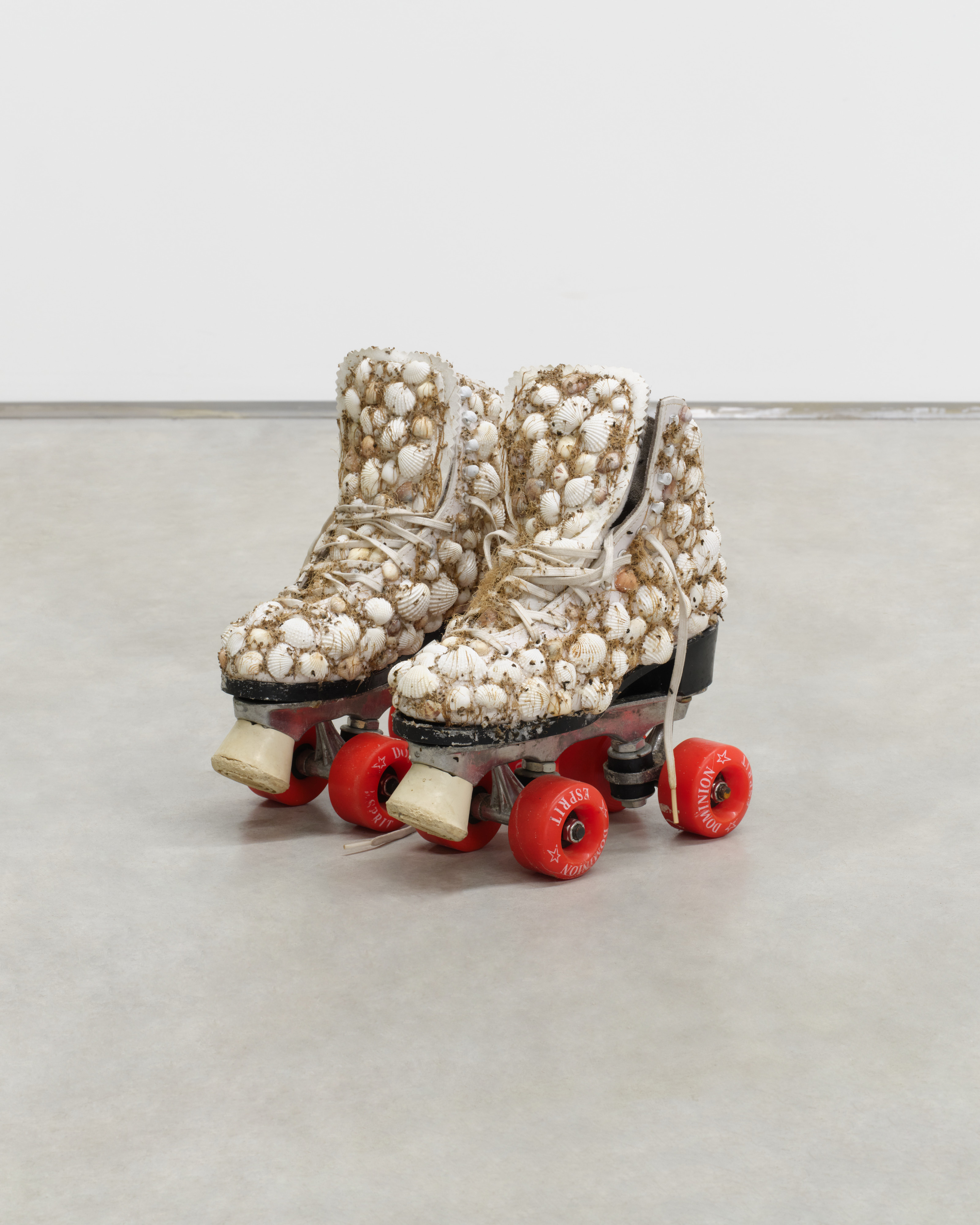 A pair of roller skates covered in seashells and dried grasses. 