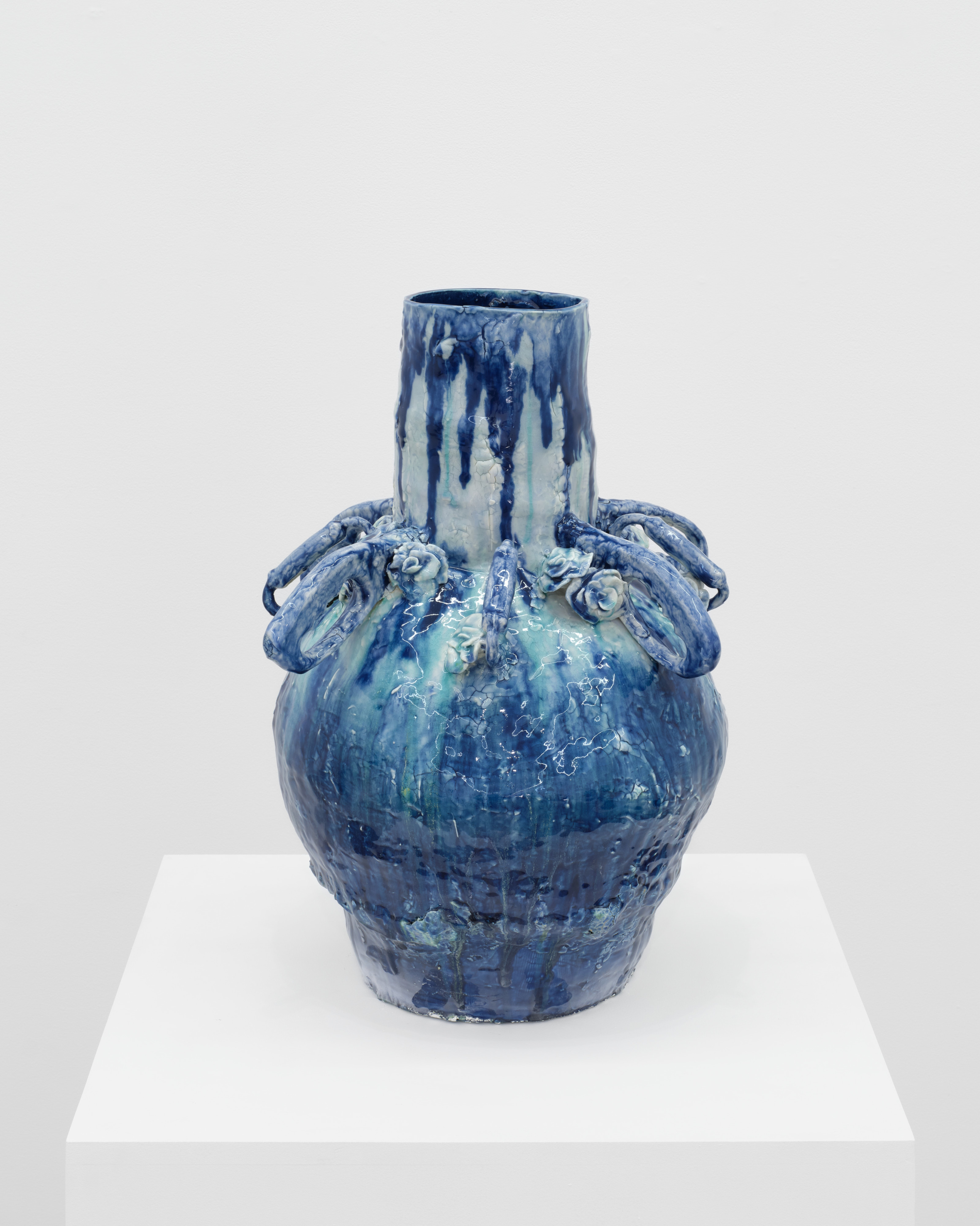 A gradient blue vessel with a tapered opening and a round base with floral shapes around the base.