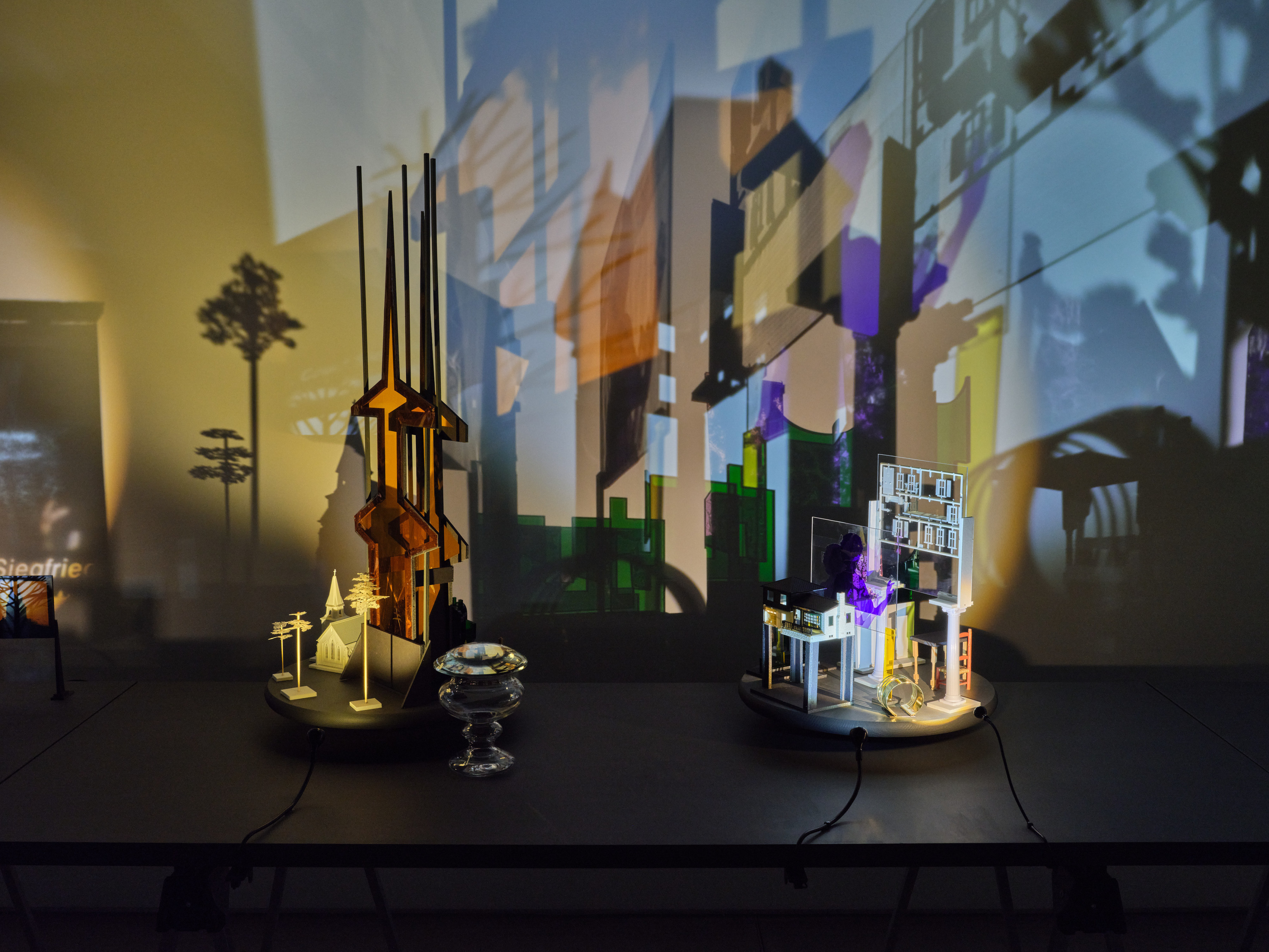 Two table top sculptures comprised of miniature trees, miniature churches, colored plexiglass steeples, upside down crystal vessels with shadows that project onto the walls surrounding.