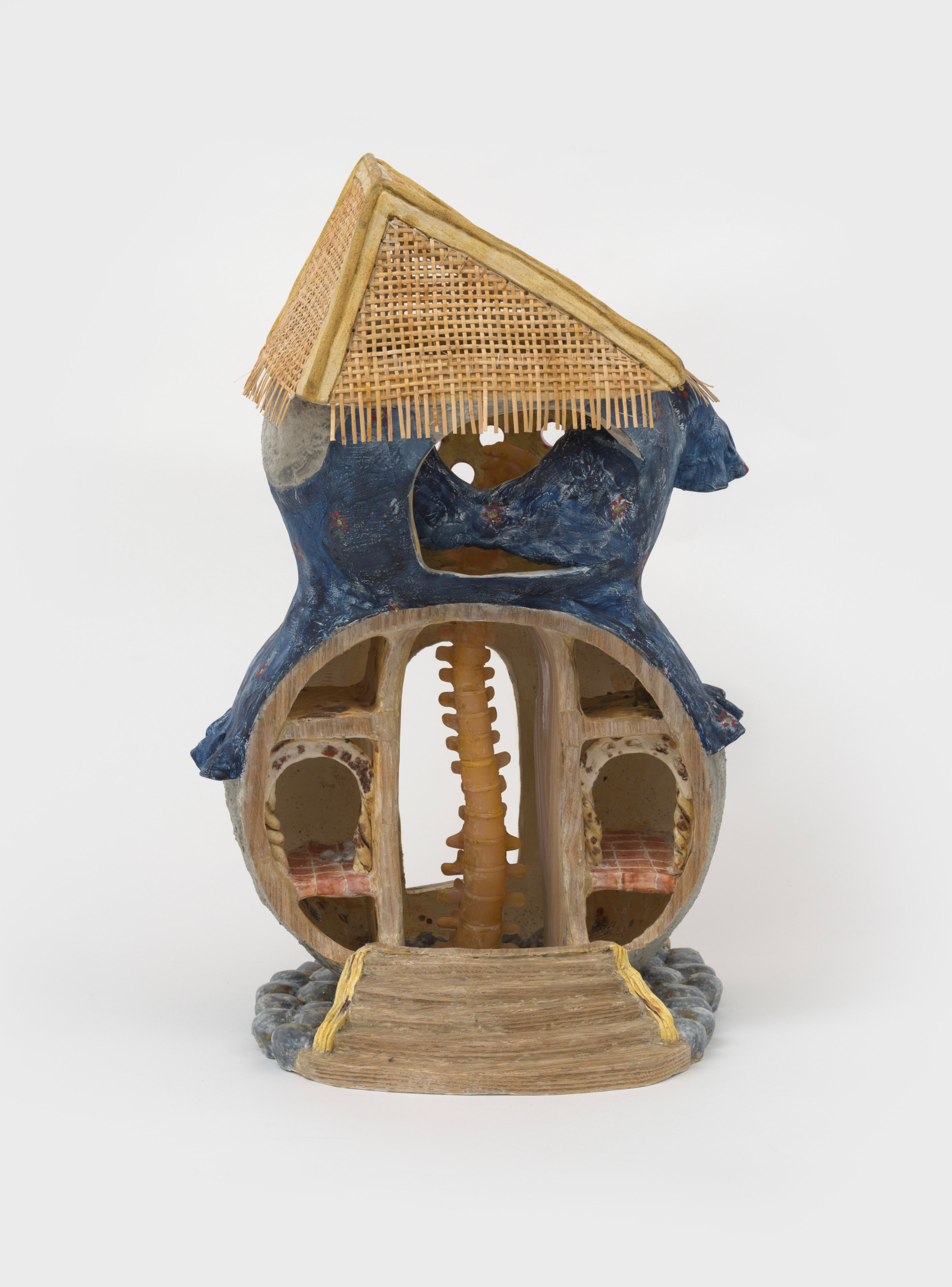 An 18 inch tall ceramic sculpture of a rounded two story house like form with a blue exterior, a woven triangular roof and a spinal cord through the center of the interior. 