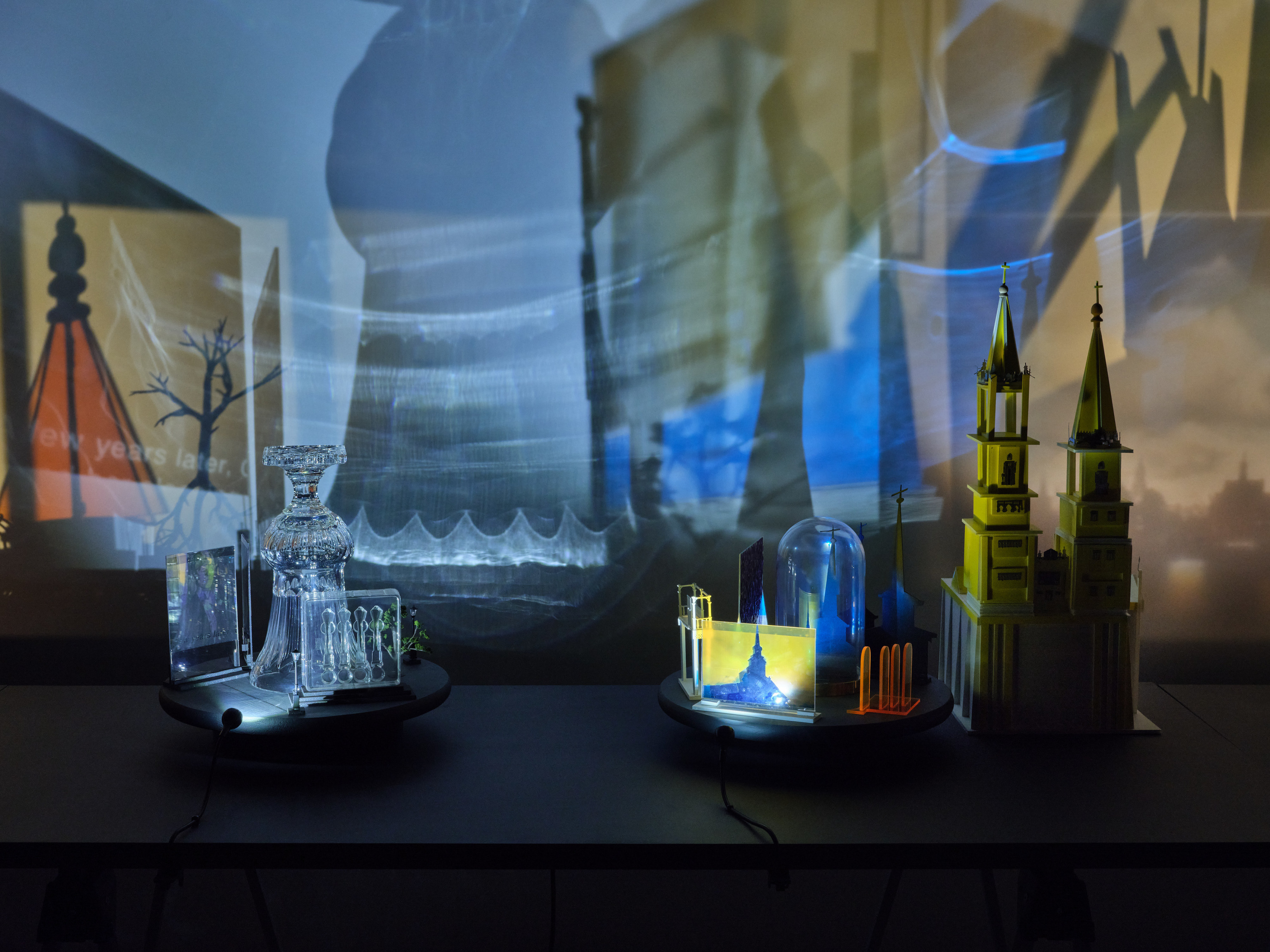 A series of assemblage sculptures comprised of upside down crystal vases, miniature street lamps, photographs printed on plexiglass and steeples made from styrene atop rotating platforms.