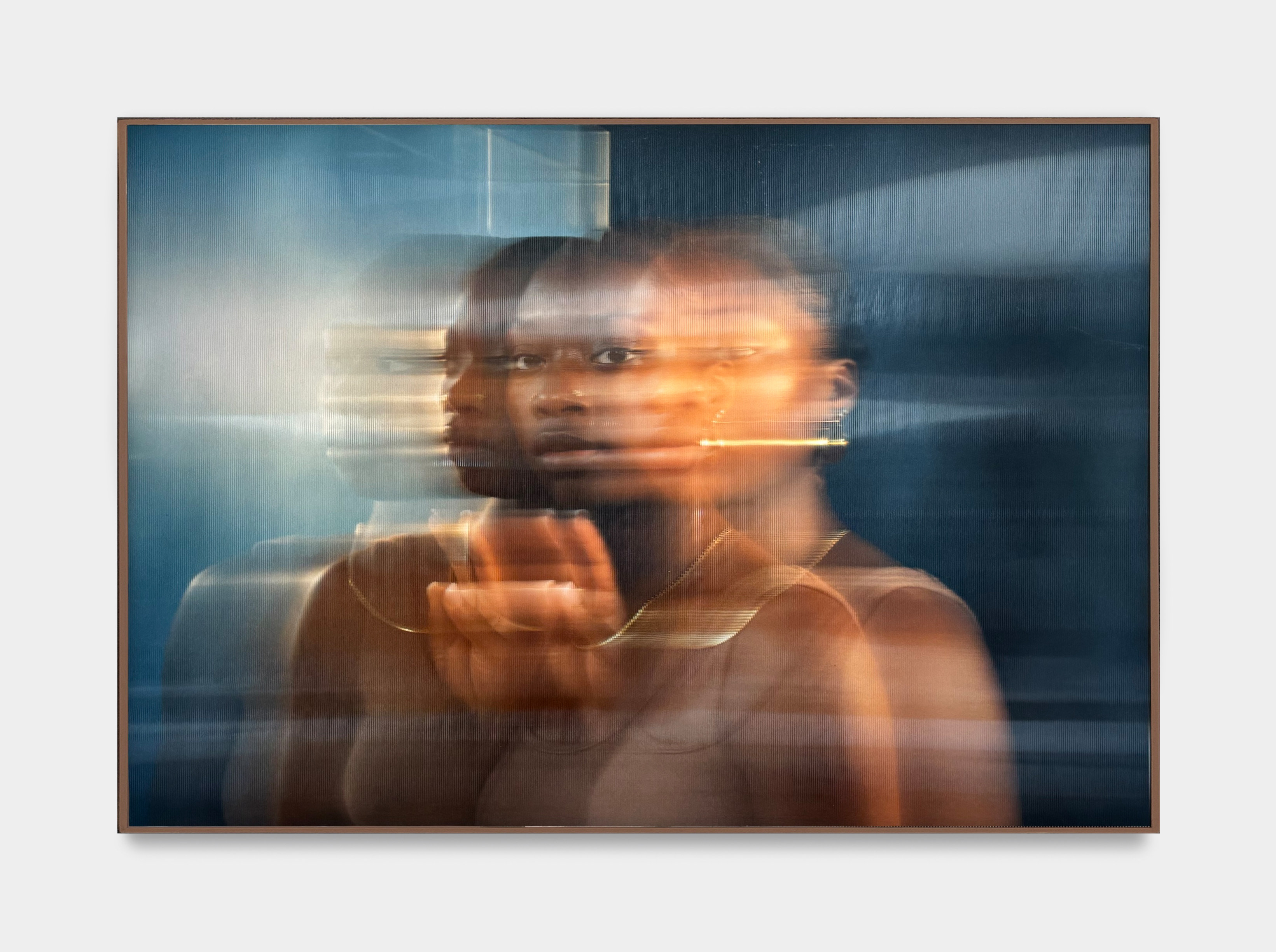 A photo by Kenturah Davis mounted on lenticular glass of a woman in gold jewelry reflected against a blue wall.