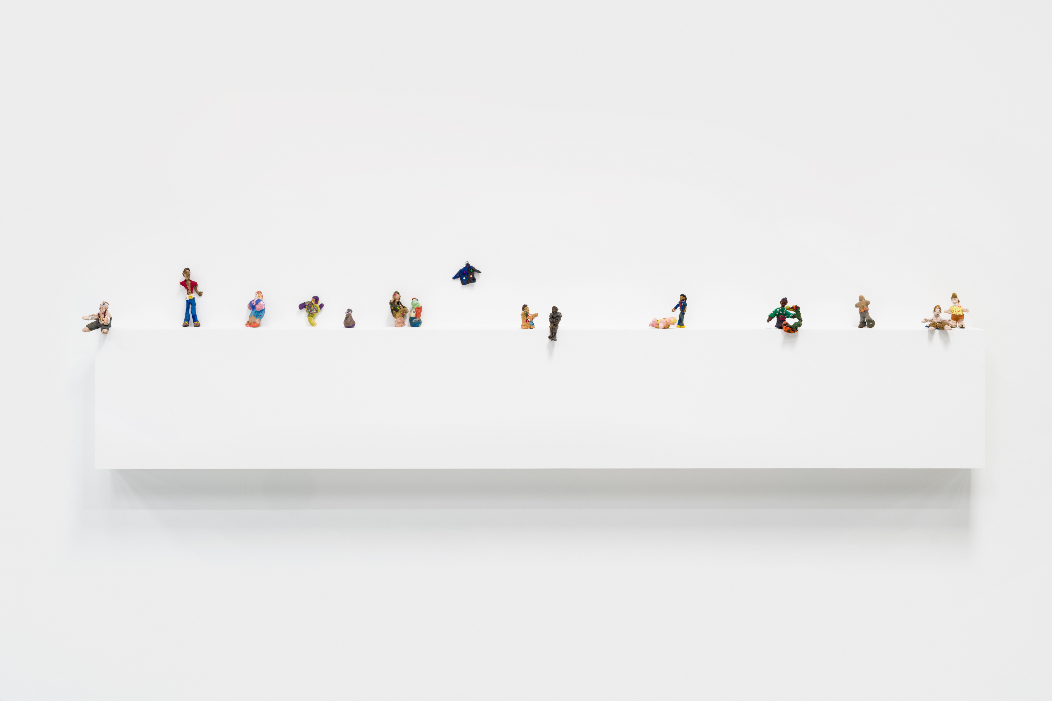 A white shelf with small sculptures of figures by Asher Hartman.