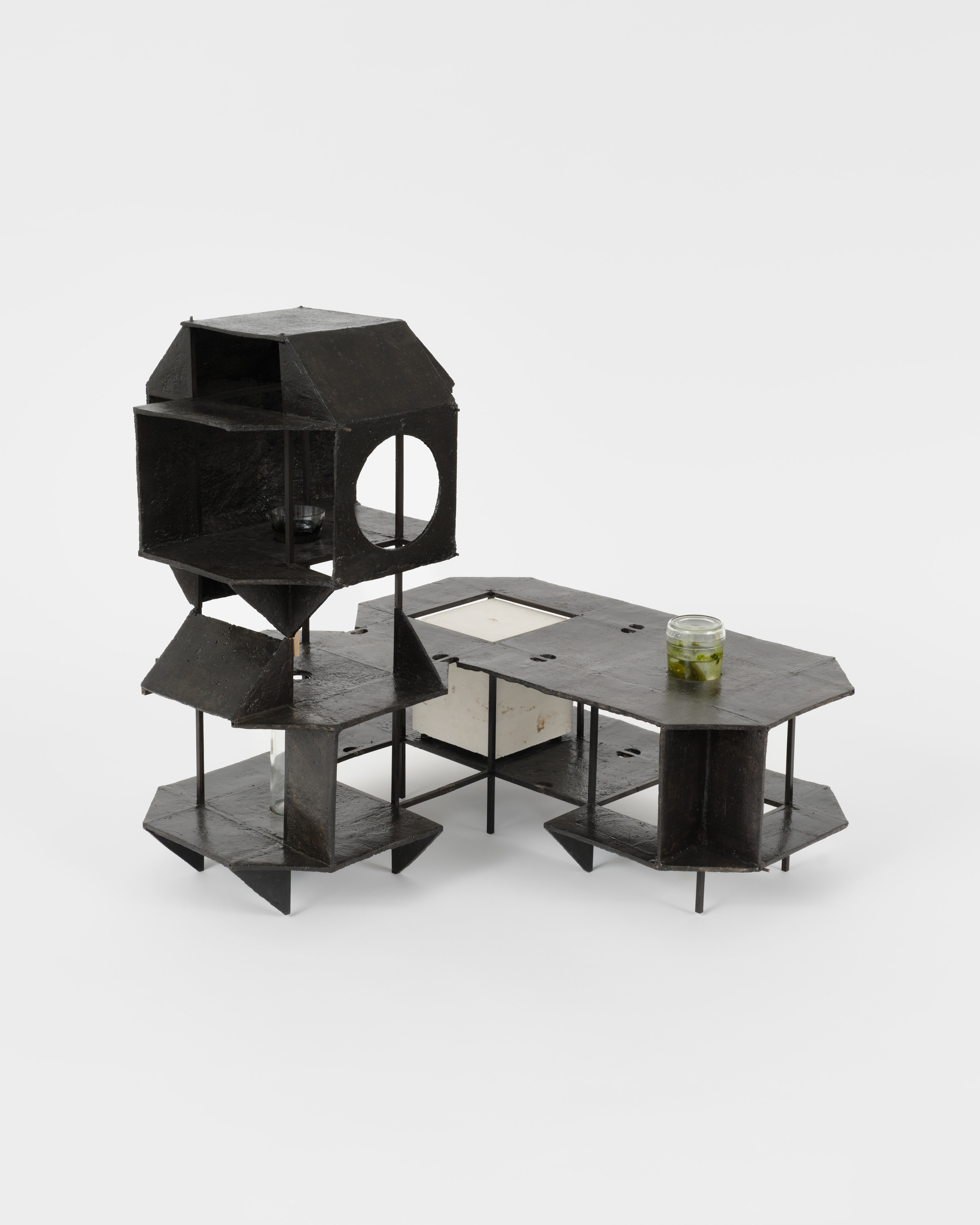 A sculpture by Alice Könitz of a small black three tiered platform with murky water in a glass jar.