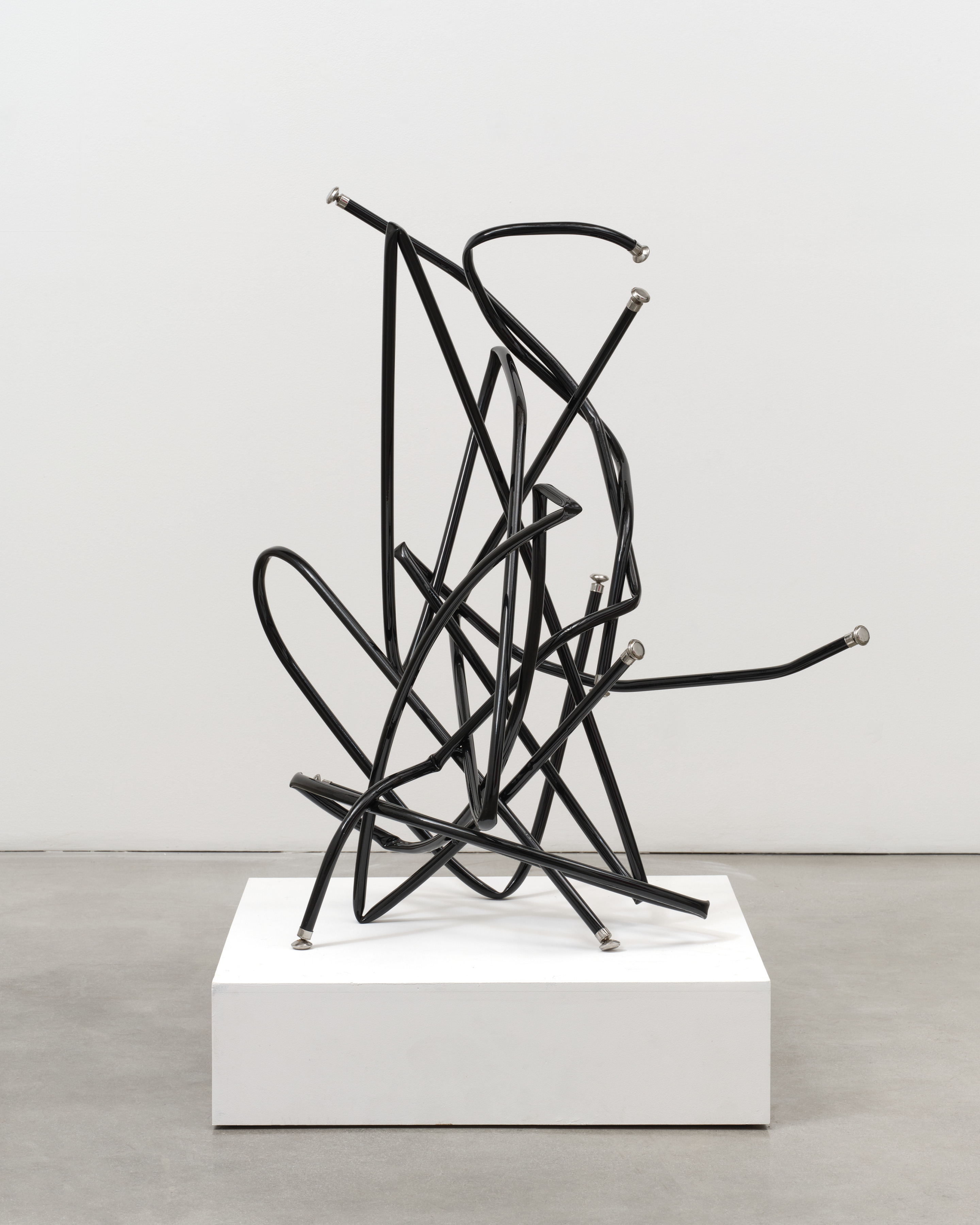 A freestanding sculpture by Josh Callaghan of black metal tubing with chair leg caps entangled and extending in all directions.