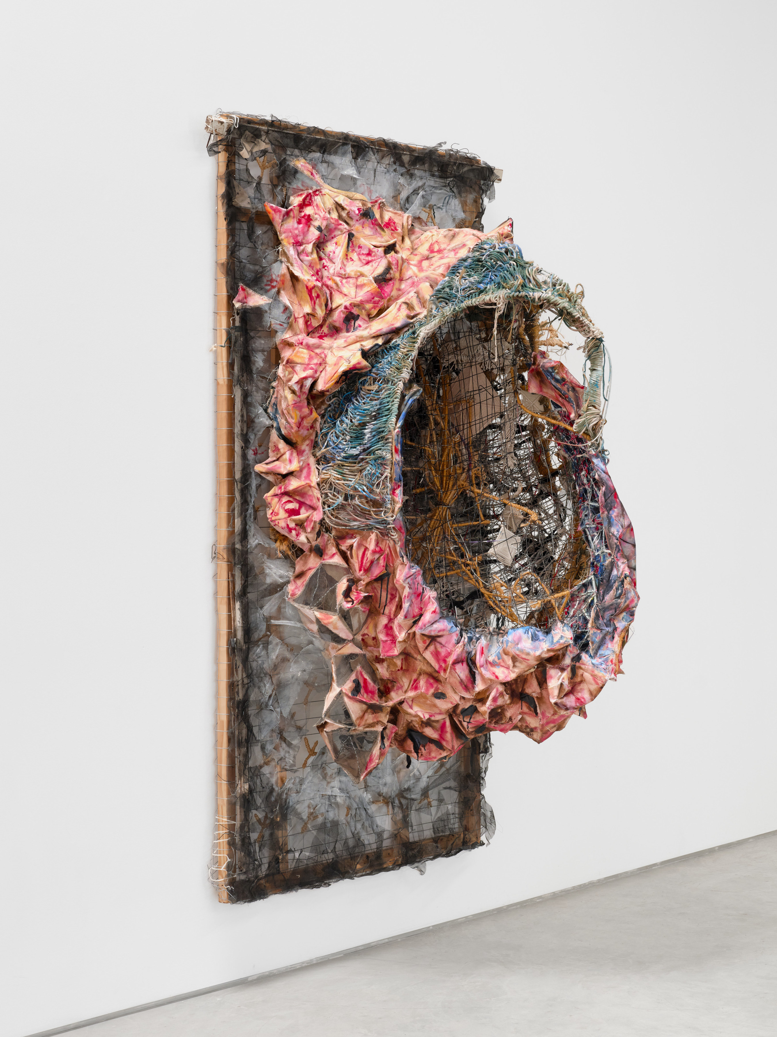 A wall mounted sculpture by Marwa Abdul-Rahman of a wire bed frame covered in canvas and twine with a nest like form protruding from the center. 