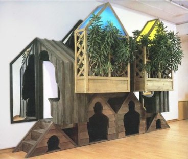 wooden installation of what looks like a house with plants growing from the front