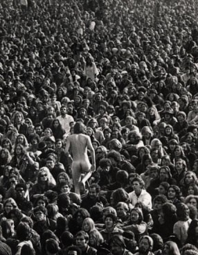 a crowd of people facing one way while a naked man faces the opposite direction