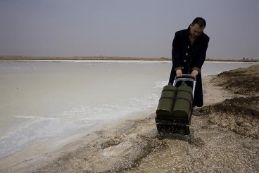 man dragging metal object through the beach