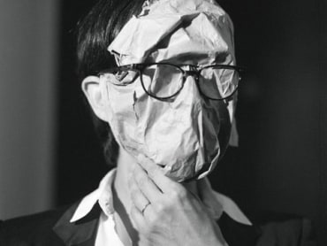 A person with a piece of paper affixed to their face wears eyeglasses on top of the paper.