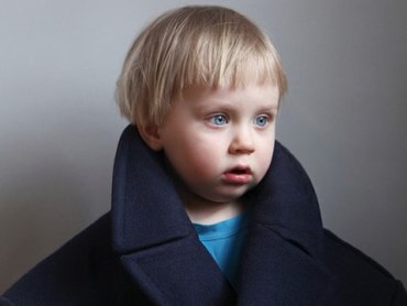 A young blond child wears an oversized coat in this color portrait.