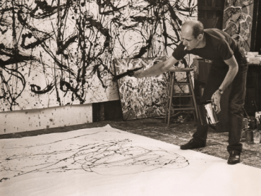 Black and white image of Jackson Pollock dribbling paint onto a canvass on the floor while smoking