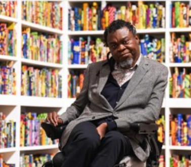 Yinka Shonibare sitting in front of a book case, which is one of his artworks 