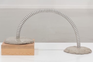 B. Wurtz sculpture of bent metal in cement with one side elevated on wood block