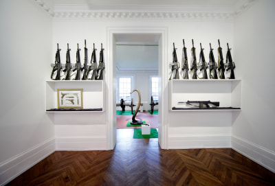 &quot;D&eacute;cor: A Conquest&quot; (XXth Century Room), 1975, One light reflector (with red light), one small green parasol, garden table with one striped blue parasol displaying one jigsaw puzzle with box, four white garden chairs with matching cushions, one AR 15 Rifle, one hand grenade revolver Smith and Wesson Mod. 36 (in vitrine), five AR 15, three FN Rifles M16, a framed print of German Luger, fourteen assorted pistols (one colt Frontier, Beretta, Colt official Police, Snub Magnum, Chief Special, Walther P 38, two Chief Specials, one Tokarev T 33 / Luger, five AR15, two FN rifles (in vitrine).