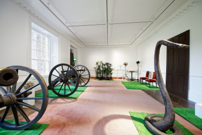 &quot;D&eacute;cor: A Conquest&quot; (XIXth Century Room), 1975, One flower ball on wooden pedestal, ten grass mats, eight palm trees, one colour photograph of a cowboy film, two wooden barrels (labeled &lsquo;GIN&rsquo; and &lsquo;RUM&rsquo;), two silver-plated candelabras on two iron plinths with wooden tops, two red velvet Edwardian chairs, four light reflectors (one red and three green), one stuffed python, one XIXth-century pistol on wooden pedestal, one circular table with green felt displaying one miniature pack of cards, one plastic crab, and one plastic lobster, two Waterloo-style cannons.