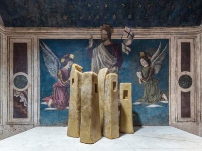 wax tower sculptures in front of frescoes depicting Christ and two angels