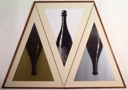 Geometric triptych of champagne bottles in triangular frames.