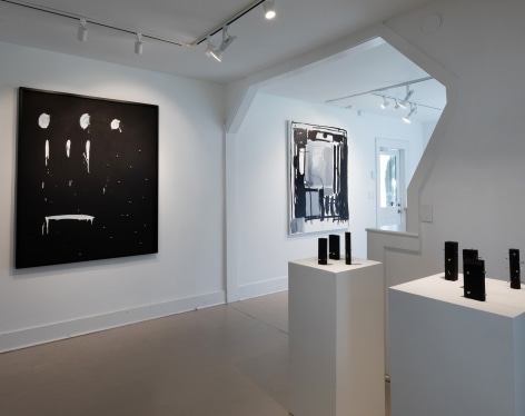 Gallery installation view of several abstract paintings and small wooden sculptures 