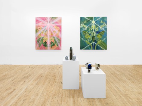 One pink and one green-tone painting are on the wall behind. Two pedestals with sculptures on top are in the front. One sculpture is placed on the left pedestal, with three decorated, sparkling meteor hammers attached to one metal item in the center. Three sculptures in the shape of heels are placed on the right pedestal.