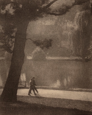 black and white image of two people walking around a pond&ndash;seen from a distance.
