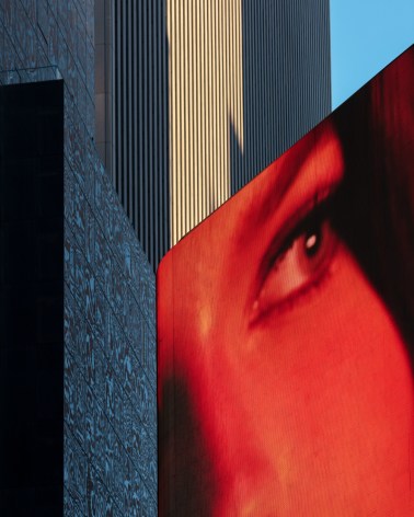 Image of a red eye diplsayed on an LCD screen in Times Square, skyscrapers and a glimpse of blue in the background.
