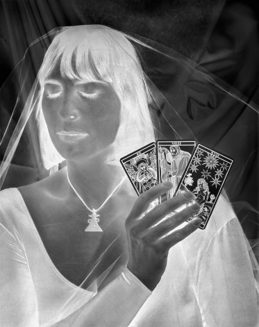 Black and white negative photograph of a veiled woman holding tarot cards.