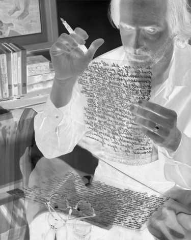 Black and white negative photograph of a man with a fountain pin reading his writing on transparent paper.