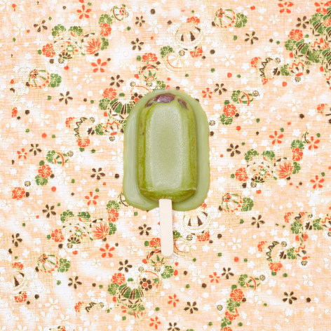 Color photo of a green popsicle melting on a patterned rice paper background.