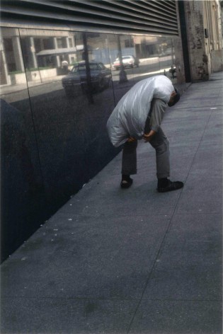 Color photograph of  hunched man with a dry cleaning bag on his back