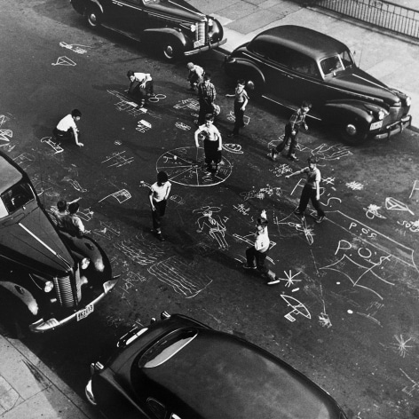 Black and white photo from above of children drawing all over a NYC street in the 1950s
