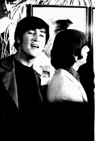 Black and white photo of John Lennon and Ringo Starr in front of a gold record and the Revolver album art enlarged on a wall.