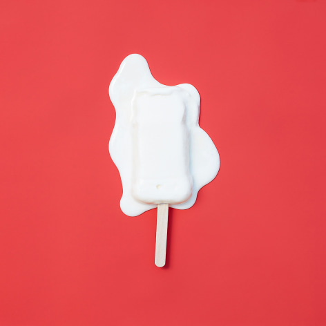 Color photo of a white popsicle melting on a red background.