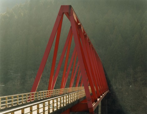 Photo of a red bridge dramatically emerging in a shaft of hazy light from a misty green hillside.