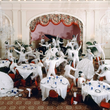 Color photograph of a staged fight by a group of fencers in a ballroom—tables that are served for dinner have been knocked over  by the fencers.