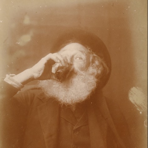 Warm toned antique photo of a bearded man drinking wine, his eye catches the camera.