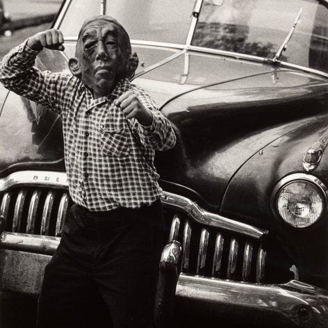 Black and white photo of an adolescent posing with fists up in a haloween mask in frint of a late 1940s Buick automobile.